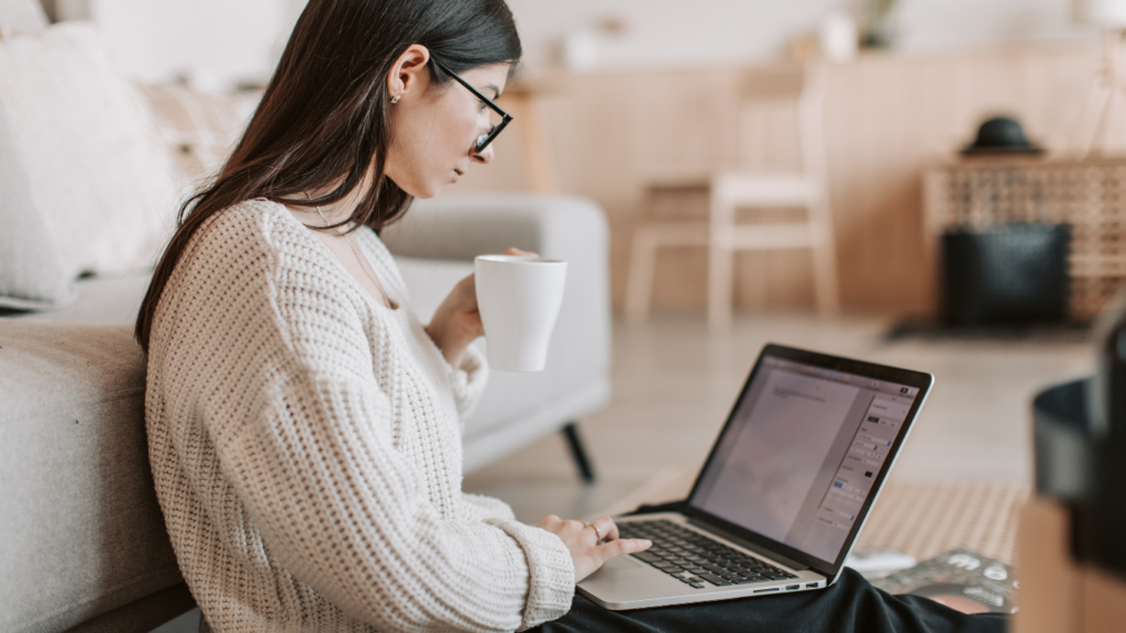 A woman using laptop while taking tea cup at home