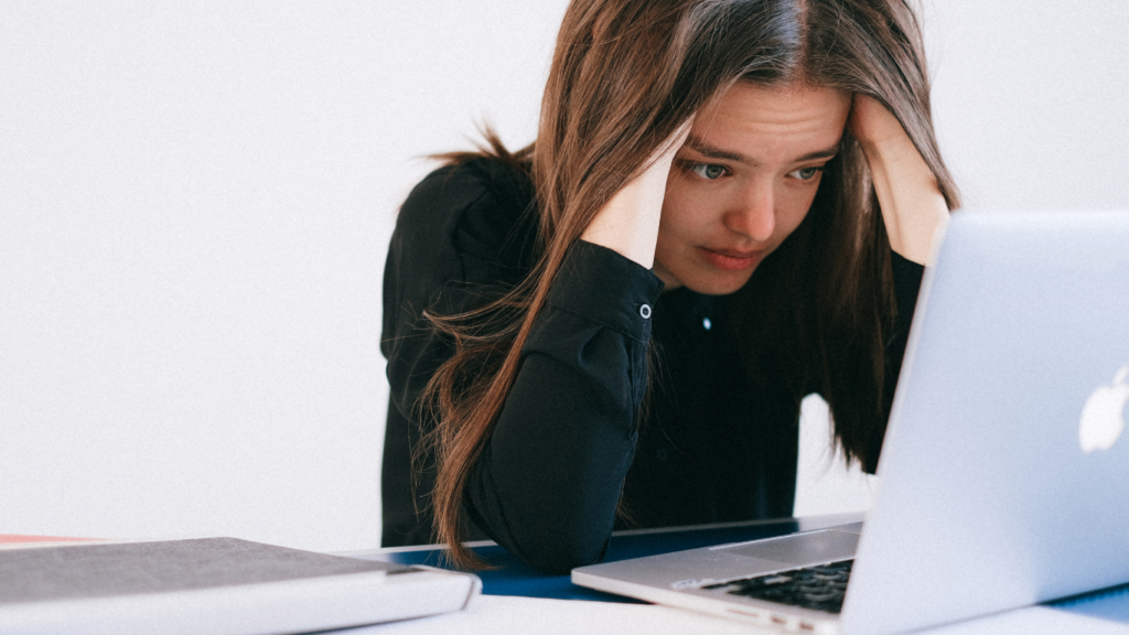 a person sitting in front of a laptop with their hands on their head